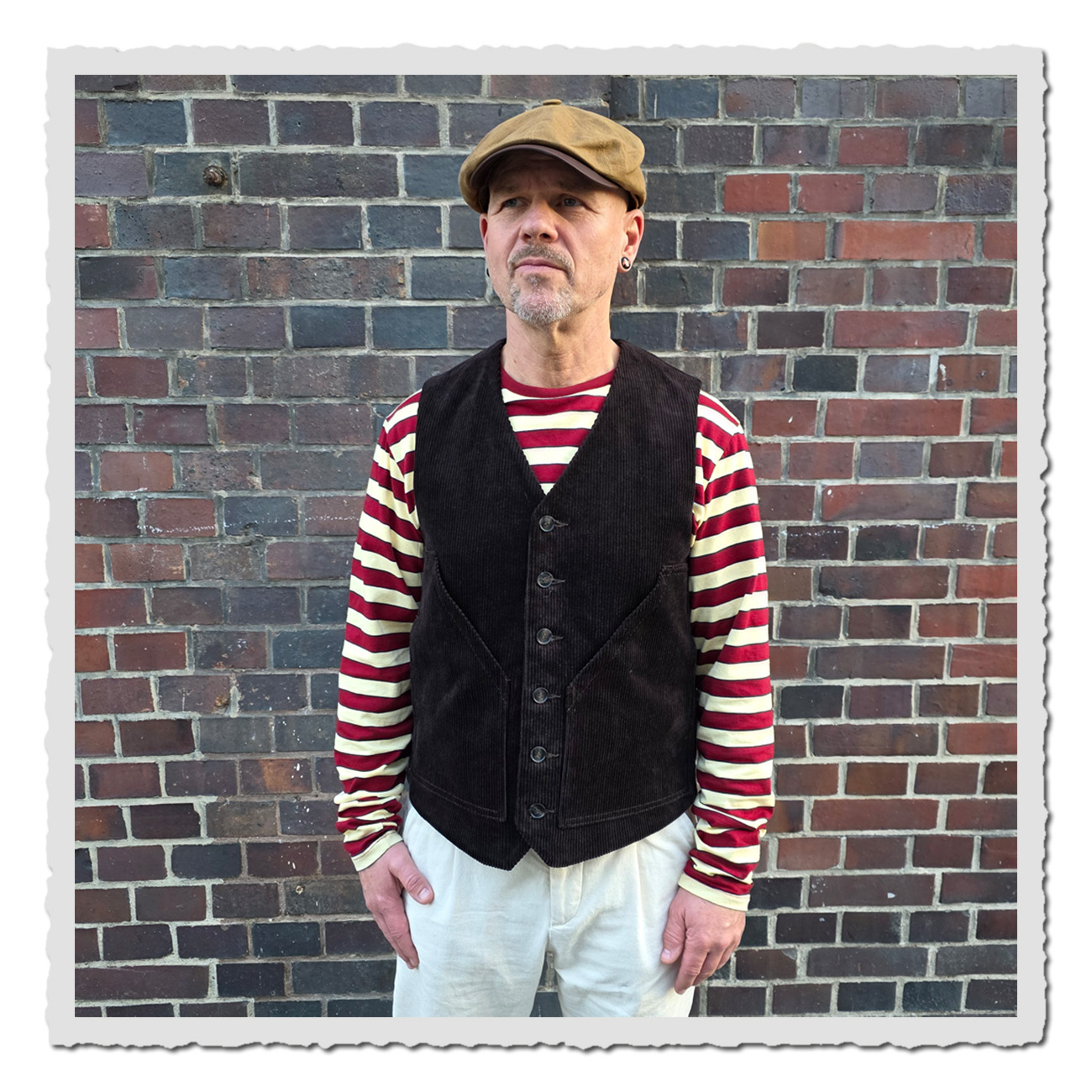 Mann vor Ziegelmauer trägt die Retronia Weste Erwin schwarzbraun – klassische Cordweste im Retro-Style